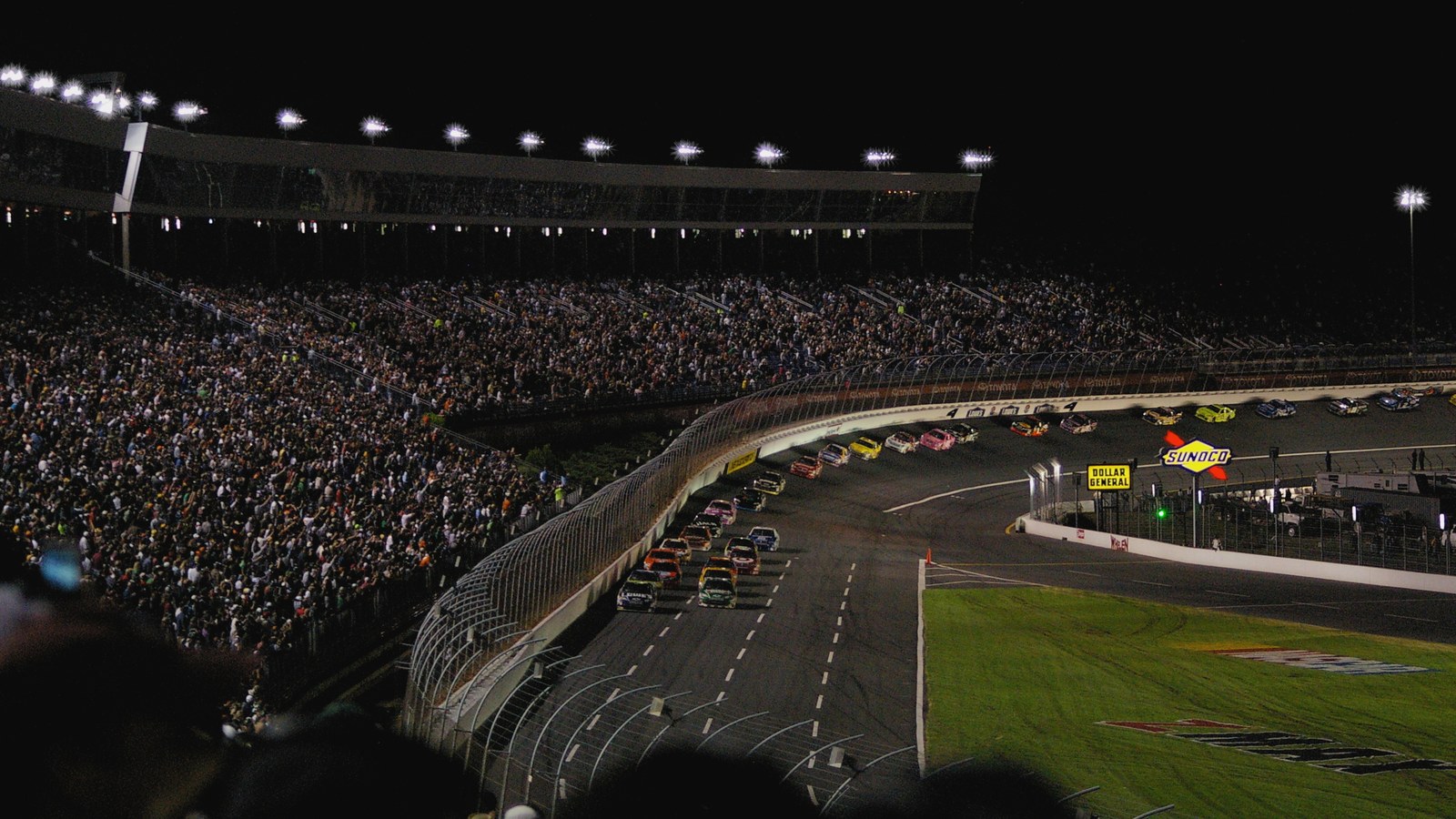 Charlotte Motor Speedway noaptea, cu mașini de curse pe viraj și tribune pline