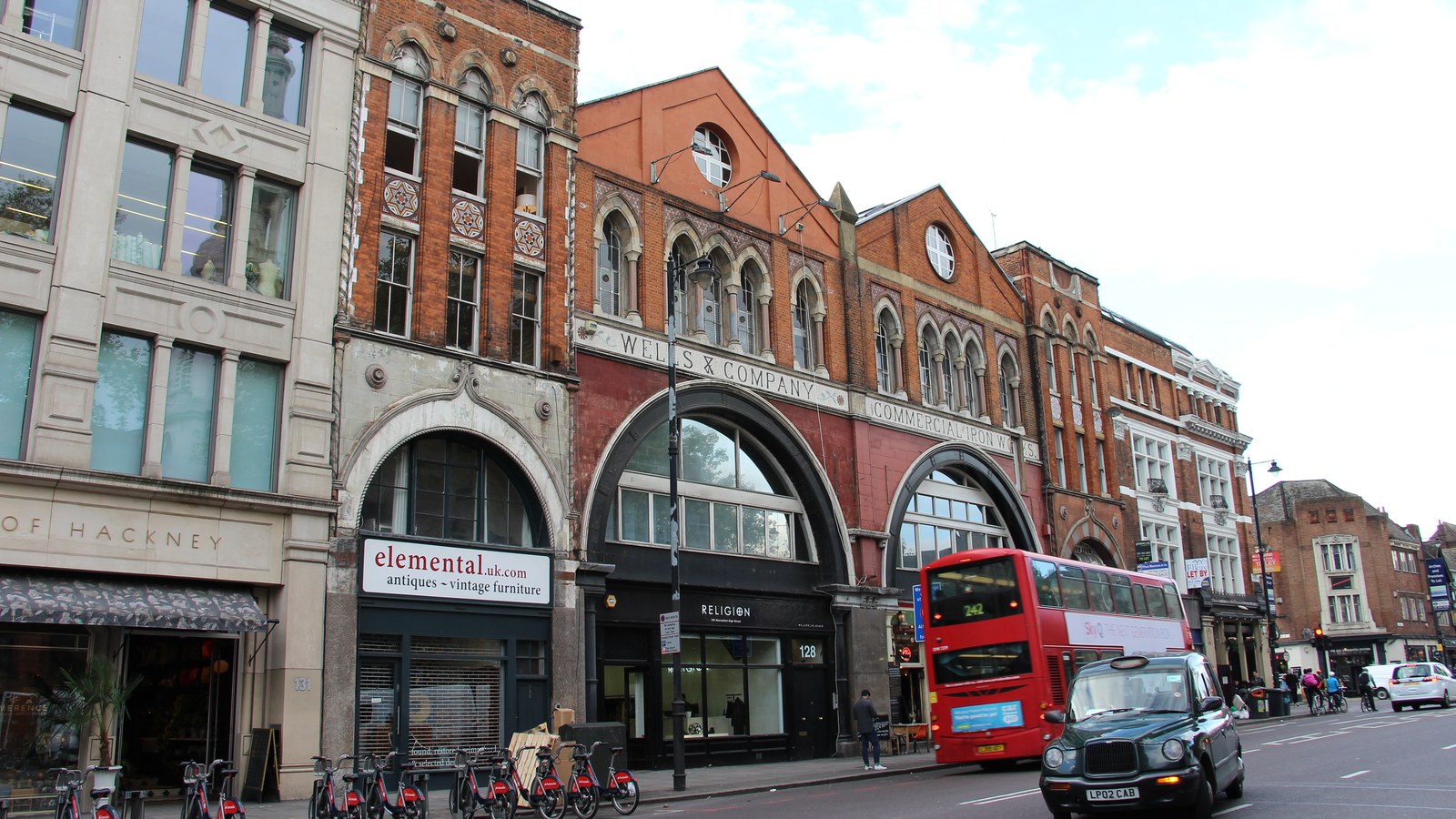 Stradă comercială pe Shoreditch High Street din Londra, cu magazine, pietoni și trafic.
