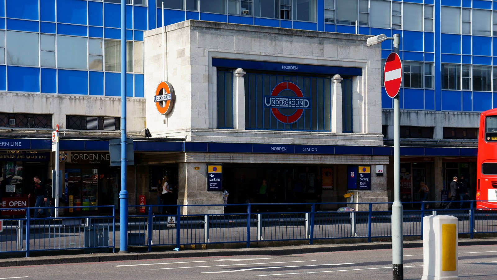 Fațada stației de metrou Morden din Londra, cu roundel-ul Underground, inscripția MORDEN STATION, magazinele de la parte…