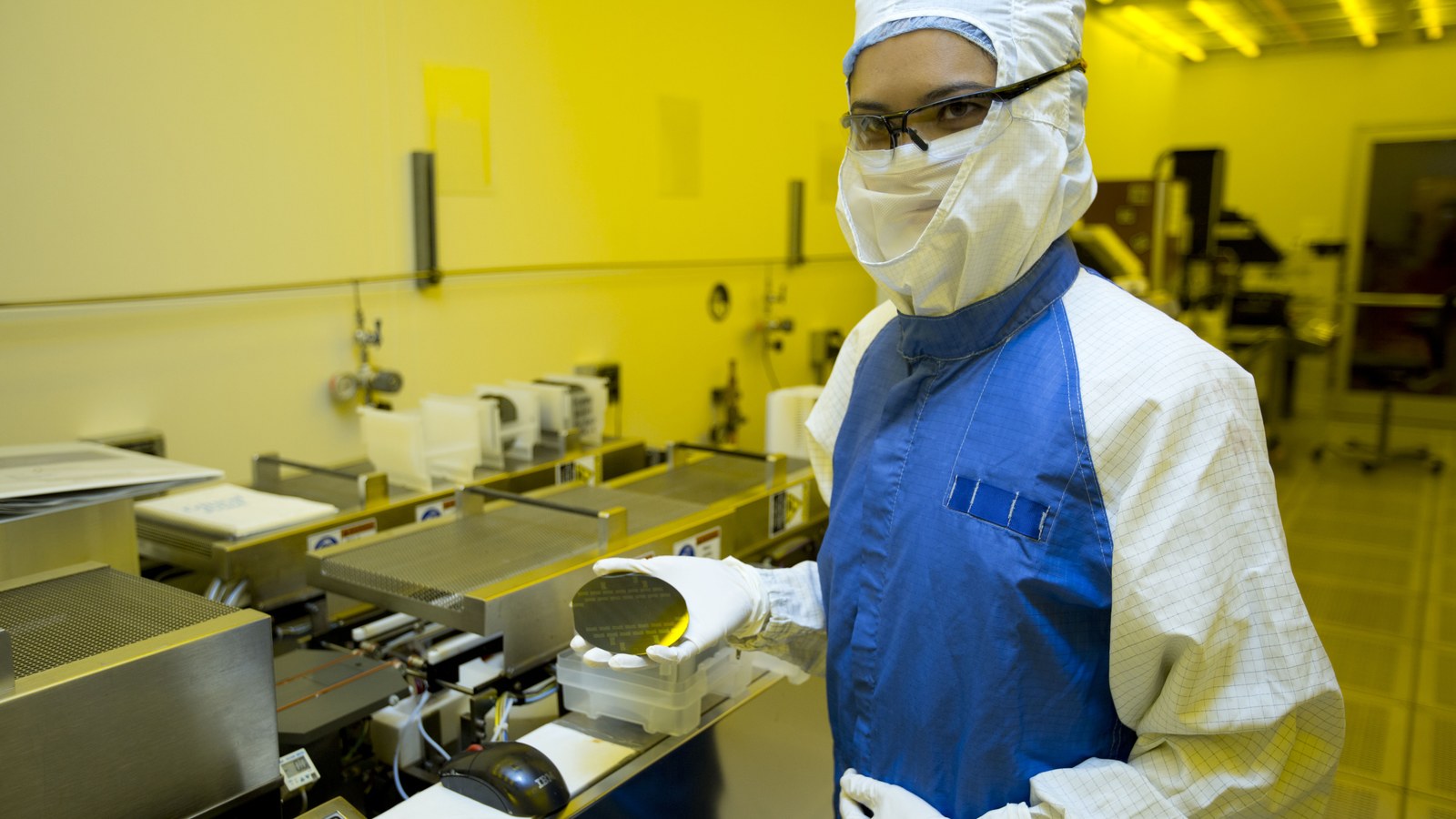 Inginer în cleanroom ținând un wafer de siliciu, infrastructură de calcul, nu un sediu OpenAI